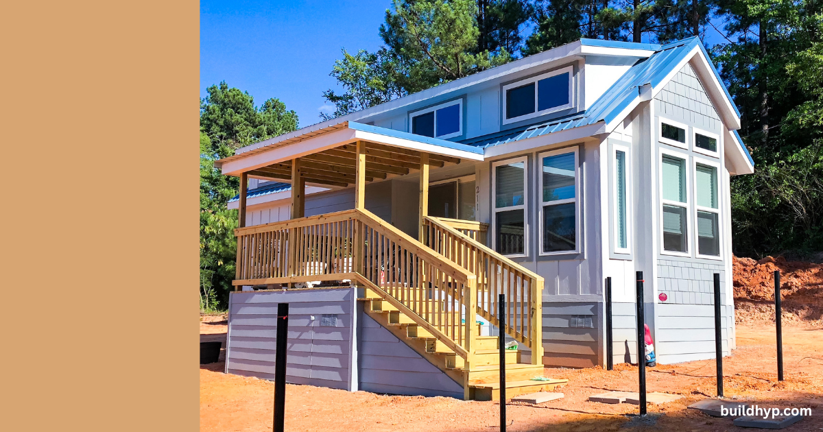 New construction two-tone tiny home with blue metal roof and inviting wooden porch, perfectly designed as compact, modern Tiny Cabin Homes nestled in a wooded landscape. See buildhyp.com for details.
