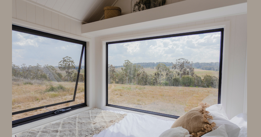 Enjoy breathtaking valley views from this cozy Summit Tiny Homes loft bedroom, featuring a plush bed with boho pillows and large corner windows. 