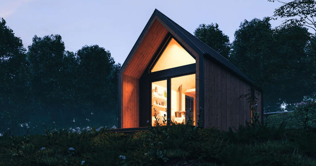 This modern, A-frame tiny home, featuring vertical cedar siding and a large glass facade, is set on a grassy hill at dusk, showcasing a cozy, warmly lit interior. 