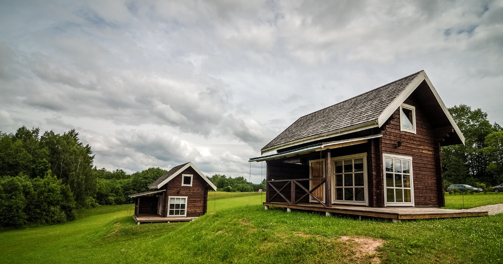 A low-angle, wide shot shows two rustic brown wooden tiny homes on wheels in a green field, illustrating the structures you can legally live in if you follow zoning laws.