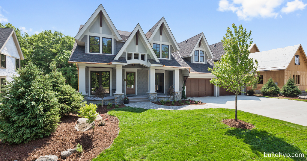 A luxury suburban mountain lodge home exterior featuring complex rooflines, dark wood paneling, white column entryways, and a large front yard.