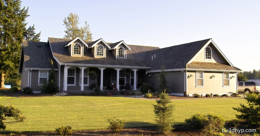 Exterior view of a gray craftsman-style mountain ranch house with gables, white trim, stone accents, and a manicured green lawn.