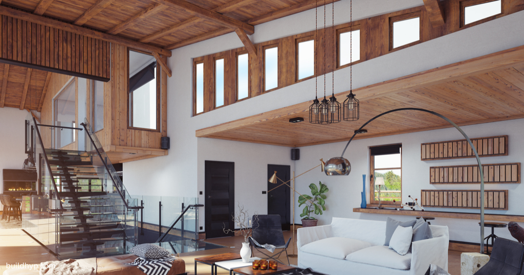 A spacious mountain lodge interior featuring high wooden beam ceilings, floor-to-ceiling windows, open stairs, and modern white couches designed into the floor plan.
