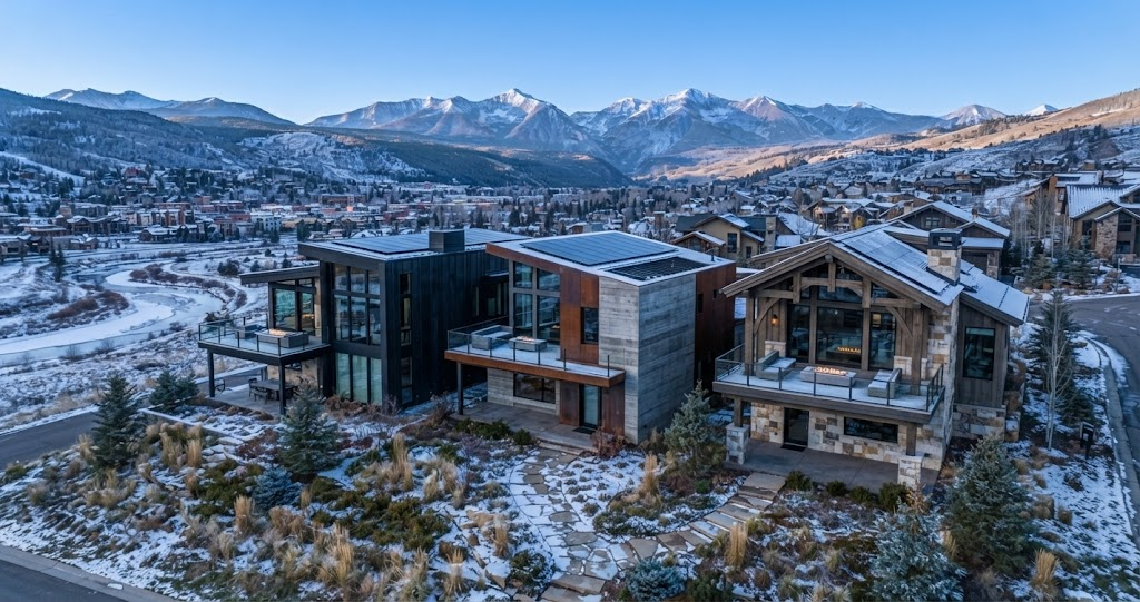 Stunning winter aerial view of luxury Colorado mountain homes in a ski resort town. Features modern and rustic designs, rooftop solar, private balconies with fire pits, and panoramic snowy peaks.