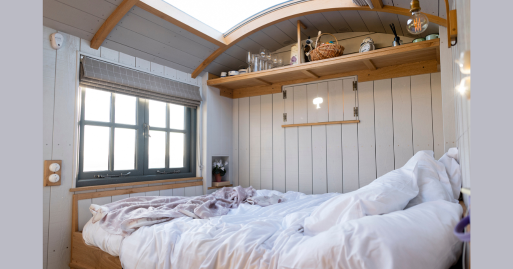 Cozy, space-saving bedroom inside modern Tiny Cabin Homes, featuring a curved skylight over a plush bed, warm wood accents, and bright natural light for compact living.